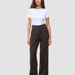 En kvinne har på seg en hvit T-skjorte og Serene Pants Wide Walnut Herringbone, som har et minimalistisk mørkebrunt design med smale striper.