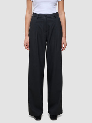 En person som har på seg de svarte Serene Pants Wide Black-buksene med plissering foran og en hvit T-skjorte i skandinavisk stil.