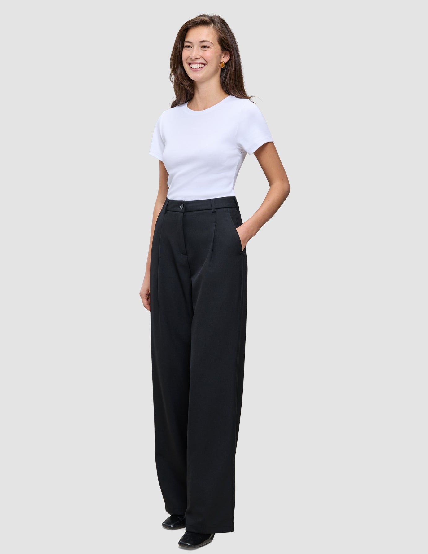 En kvinne kledd i en hvit T-skjorte og svarte Serene Pants Wide Black-bukser med høy midje og vide ben.