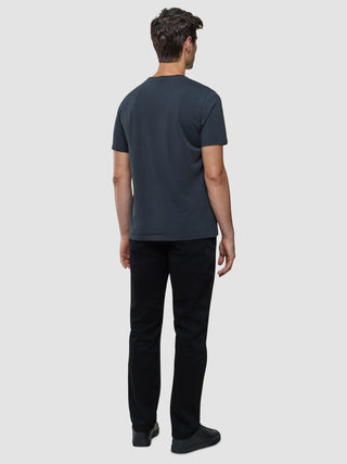 En mann sett bakfra, kledd i en Supima Legacy-T-skjorte i mørkegrått, svarte jeans og joggesko med 360°-stretch.