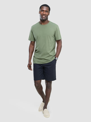 En smilende mann i en Supima-T-skjorte i fargen «Clover Green», mørke shorts og lyse loafers.