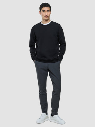 En mann kledd i en svart, hvit T-skjorte med rund hals, grå bukser og hvite joggesko i skandinavisk design.