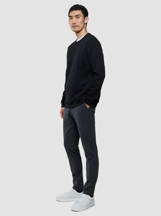 En mann kledd i en svart genser med rund hals, grå bukser og hvite joggesko.