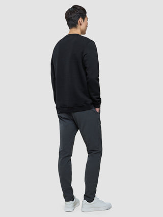 En mann sett bakfra, kledd i en svart sweatshirt med rund hals, mørke bukser og hvite joggesko.