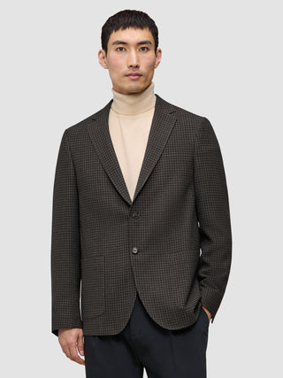 En mann som har på seg en Timeless Wool Blazer Slim i mørkebrun rutemønster over en beige turtleneck-genser.