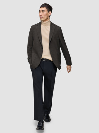 En mann kledd i en Timeless Wool Blazer Slim i mørkebrun rutemønster, beige turtleneck, svarte bukser og loafers.
