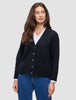 En kvinne som har på seg en svart, grovstrikket, myk ullcardigan for kvinner over en hvit skjorte med krage og blå jeans.