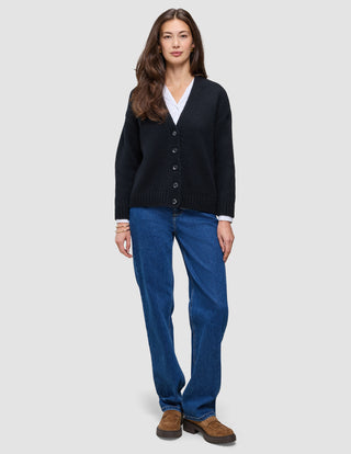 En person som har på seg en svart, grovstrikket, myk ullcardigan for kvinner over en hvit skjorte og blå jeans.