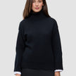 En person har på seg en svart, tykk og myk ullstrikket turtleneck for kvinner med vide ermer over en hvit skjorte.