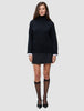 En person som har på seg en svart, tykk og myk ullstrikket turtleneck for kvinner over en hvit skjorte, et svart skjørt og gjennomsiktige knestrømper.