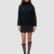 En person som har på seg en svart, tykk og myk ullstrikket turtleneck for kvinner over en hvit skjorte, et svart skjørt og gjennomsiktige knestrømper.
