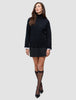 En kvinne har på seg en svart, tykk og myk ullstrikket turtleneck for kvinner over en hvit skjorte med krage, et svart skjørt og svarte høyhælte sko.