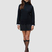 En kvinne har på seg en svart, tykk og myk ullstrikket turtleneck for kvinner over en hvit skjorte med krage, et svart skjørt og svarte høyhælte sko.