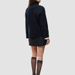 En person sett bakfra, kledd i en svart, tykk og myk ullstrikket turtleneck for kvinner, svart skjørt og gjennomsiktige knestrømper.