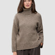 En kvinne iført en taupefarget, grovstrikket turtleneck i myk ull for kvinner, i fargen Taupe Melange.