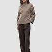 En kvinne kledd i en tykk, myk ullstrikket turtleneck for kvinner i fargen taupe melange og bukser med vid benvidde og smale striper.