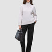 En kvinne i en lys turtleneck og Women GO2 Pants Straight Black, som holder en håndveske i minimalistisk skandinavisk stil.