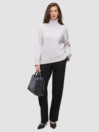 En kvinne i en lys turtleneck og Women GO2 Pants Straight Black, som holder en håndveske i minimalistisk skandinavisk stil.