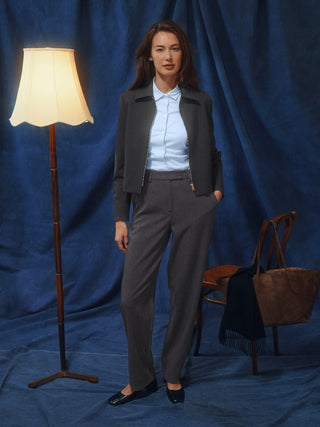 En kvinne har på seg en mørkegrå jakke, en lyseblå skjorte med knapper og Women GO2 Pants Straight Dark Grey Melange.