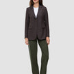 En kvinne i en brun blazer med smale striper, hvit T-skjorte, Women GO2 Pants Straight i fargen Dusty Olive og mørke loafers.