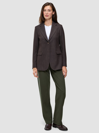 En kvinne i en brun blazer med smale striper, hvit T-skjorte, Women GO2 Pants Straight i fargen Dusty Olive og mørke loafers.