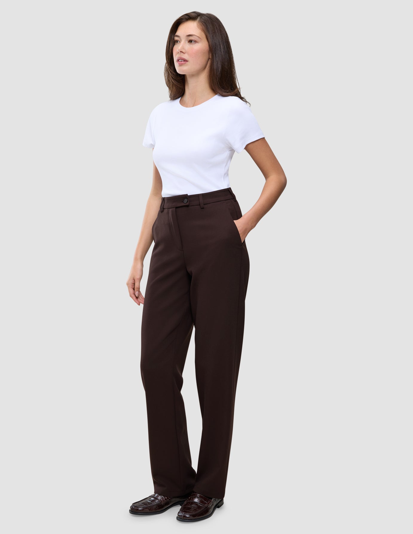 En kvinne i en hvit T-skjorte og et par Women GO2 Pants Straight i fargen mocha, med hånden i lommen.