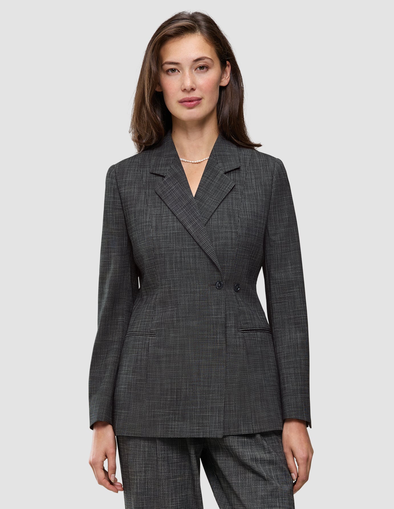En kvinne har på seg en Women Nara Blazer Fitted Black Check, en tettsittende blazer med dobbeltknapping i svart-hvitt rutemønster.