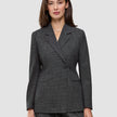 En kvinne har på seg en Women Nara Blazer Fitted Black Check, en tettsittende blazer med dobbeltknapping i svart-hvitt rutemønster.