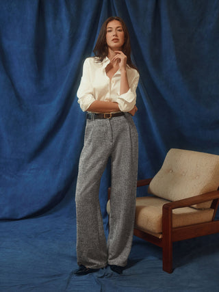 En kvinne har på seg en Women’s Oxford Shirt White Orchid Slim, som er stappet inn i grå bukser med vid benvidde i et minimalistisk design.