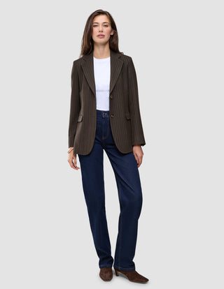 En person har på seg en brun Women Serene Blazer Regular Walnut Herringbone, en hvit T-skjorte og mørkeblå jeans.