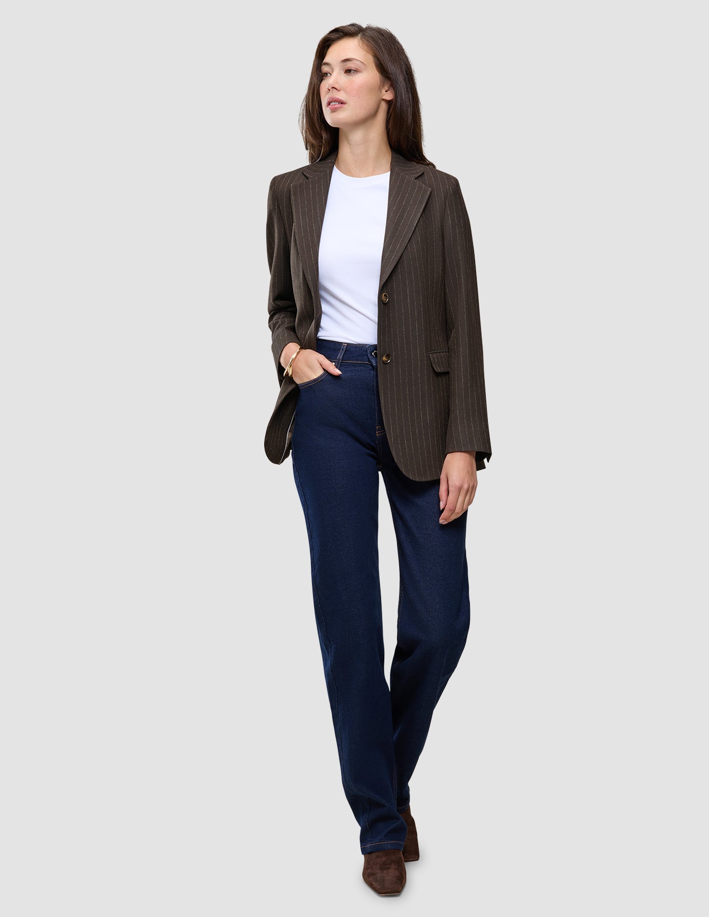 En kvinne kledd i en Women Serene Blazer Regular Walnut Herringbone, en hvit T-skjorte og mørkeblå jeans.