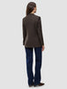 Sett bakfra har personen på seg en Women Serene Blazer Regular Walnut Herringbone, mørkeblå jeans og brune sko.