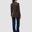 Sett bakfra har personen på seg en Women Serene Blazer Regular Walnut Herringbone, mørkeblå jeans og brune sko.
