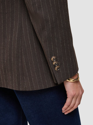 Nærbilde av en brun Women Serene Blazer Regular Walnut Herringbone-jakke med tre knapper på ermet og et gullarmbånd.