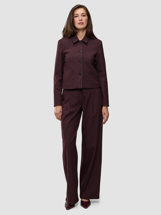 En kvinne har på seg en Women Serene Short Jacket Berry Pinstripe sammen med matchende bukser med vide ben i mørkt stoff med tynne striper.