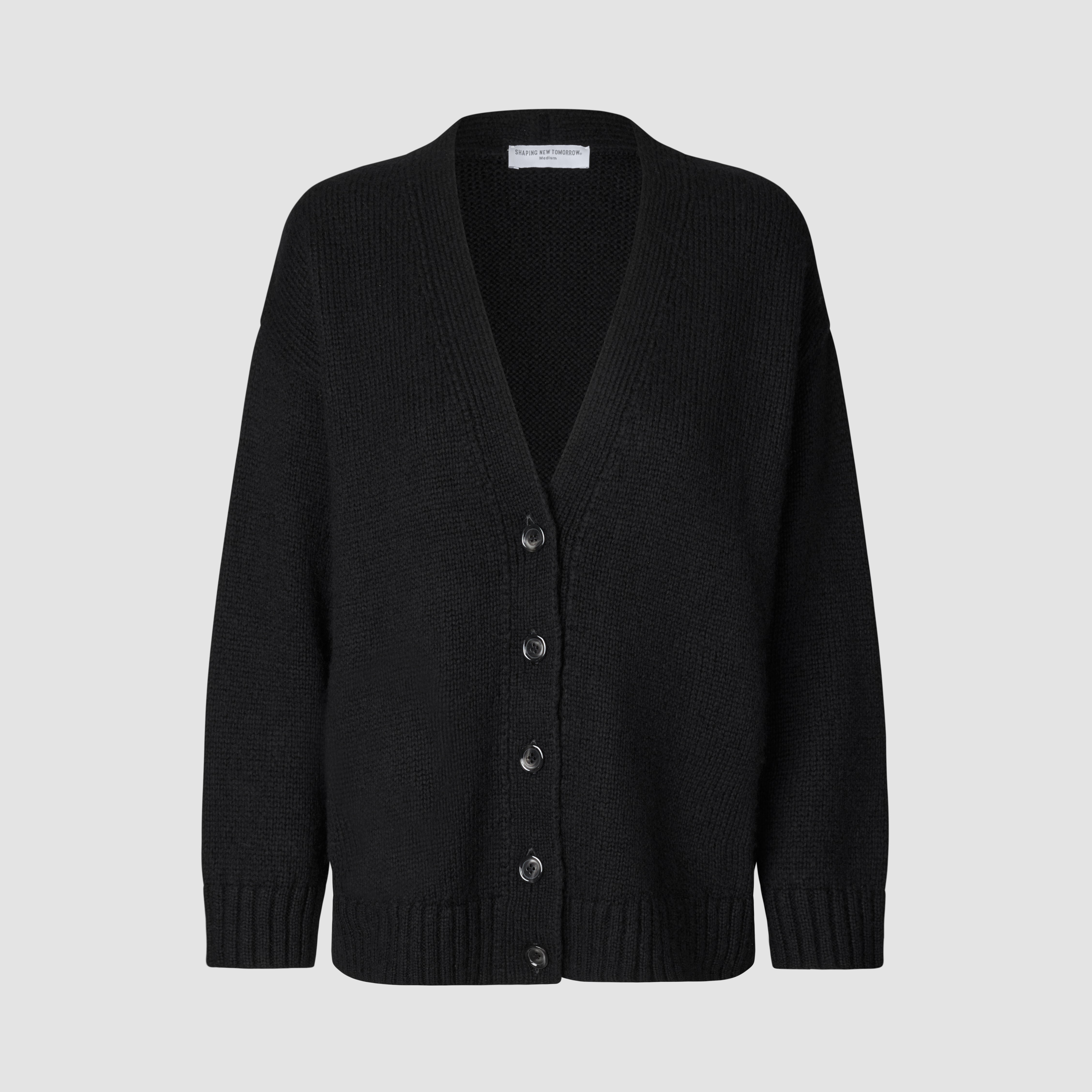 Kvinners tykk, myk ullstrikket cardigan i svart: en modell med V-hals og knapper foran, samt ribbestrikkede mansjetter og nederkant.
