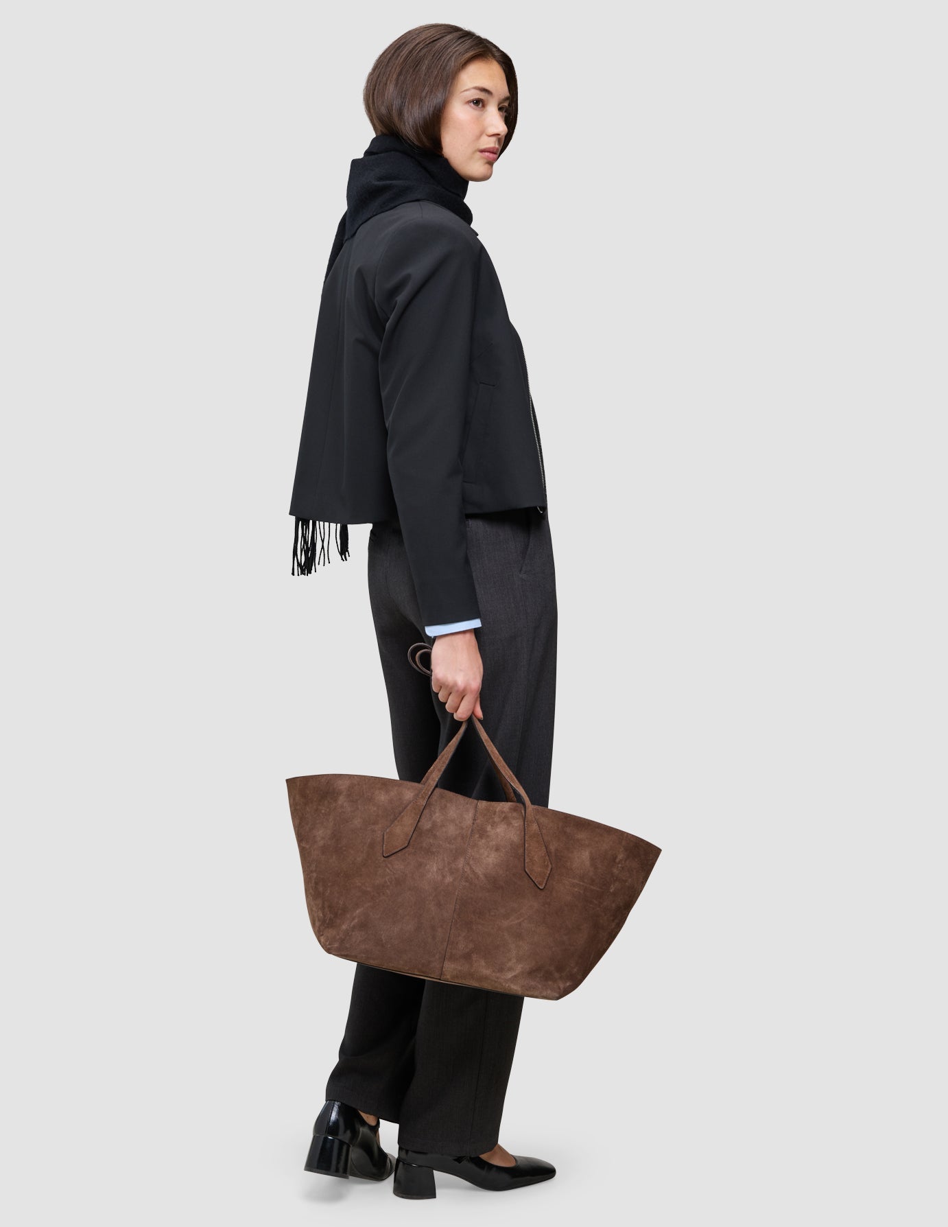 En kvinne iført en An easy office upgrade-jakke med glidelås og mørke Go2-bukser bærer en stor brun totebag.