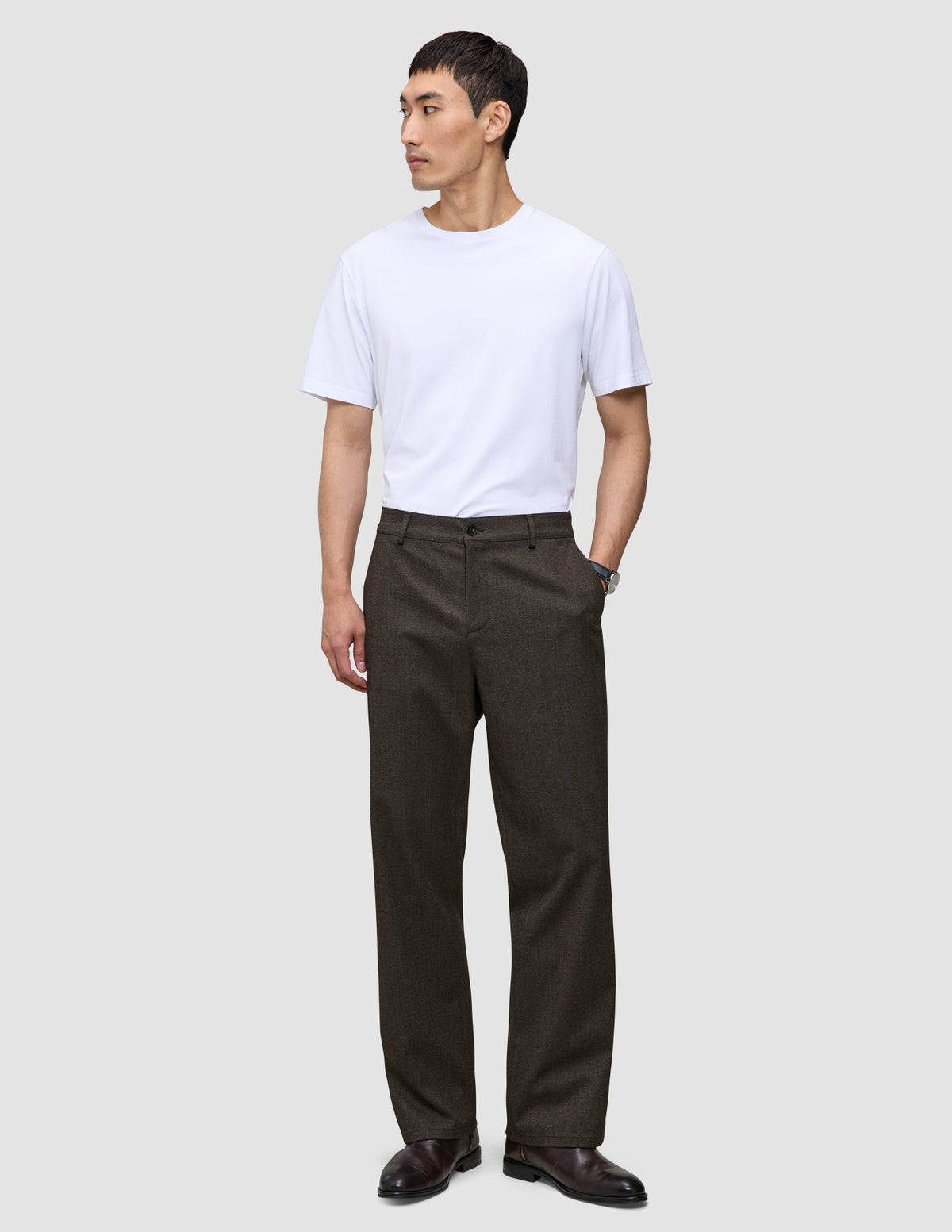 En mann i en hvit T-skjorte og Atelier Pants Relaxed Dark Brown, som gjenspeiler en stil preget av skandinavisk design.