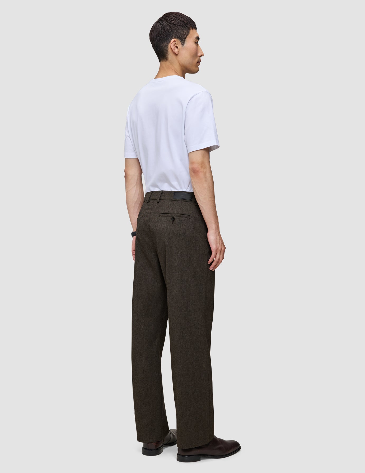 En person sett fra siden, kledd i en hvit T-skjorte og Atelier Pants Relaxed Dark Brown i brutt twill.