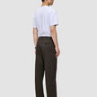 En person sett fra siden, kledd i en hvit T-skjorte og Atelier Pants Relaxed Dark Brown i brutt twill.
