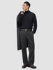 En mann i svart turtleneck og mørkegrå Atelier Pants Relaxed, med en jakke i skandinavisk design over skulderen.
