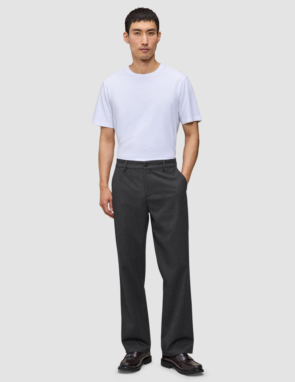 En mann i hvit T-skjorte, Atelier Pants Relaxed i mørkegrått og mørke loafers – et levende eksempel på skandinavisk design.