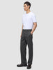 En person i en hvit T-skjorte og mørkegrå Atelier Pants Relaxed-bukser står med den ene hånden i lommen.
