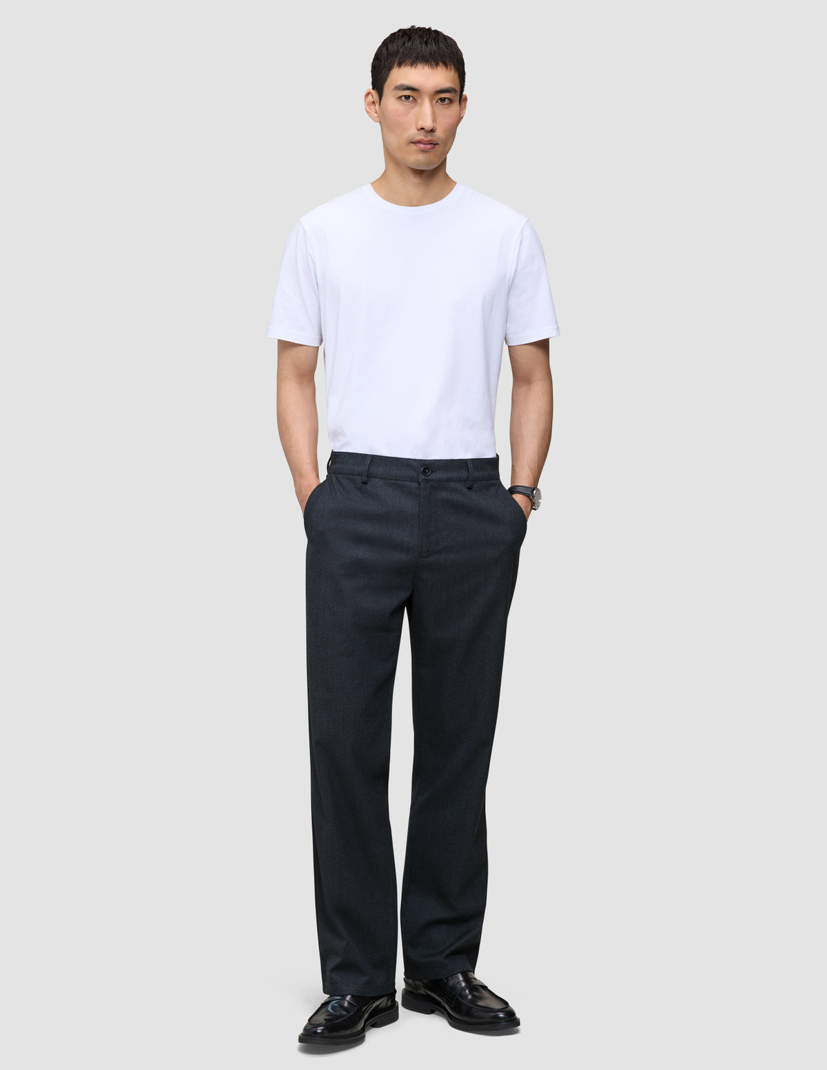 En mann i hvit T-skjorte, mørk marineblå Atelier Pants Relaxed og svarte loafers, som gjenspeiler det rene skandinaviske designet.
