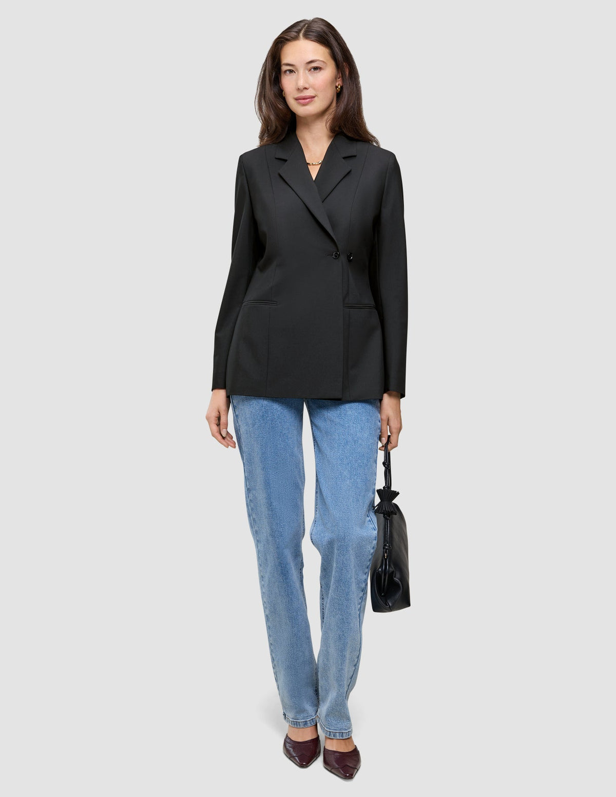 En kvinne har på seg en svart Women’s Avira Blazer Black, blå jeans og mørke høyhælte sko, mens hun holder en liten svart håndveske.