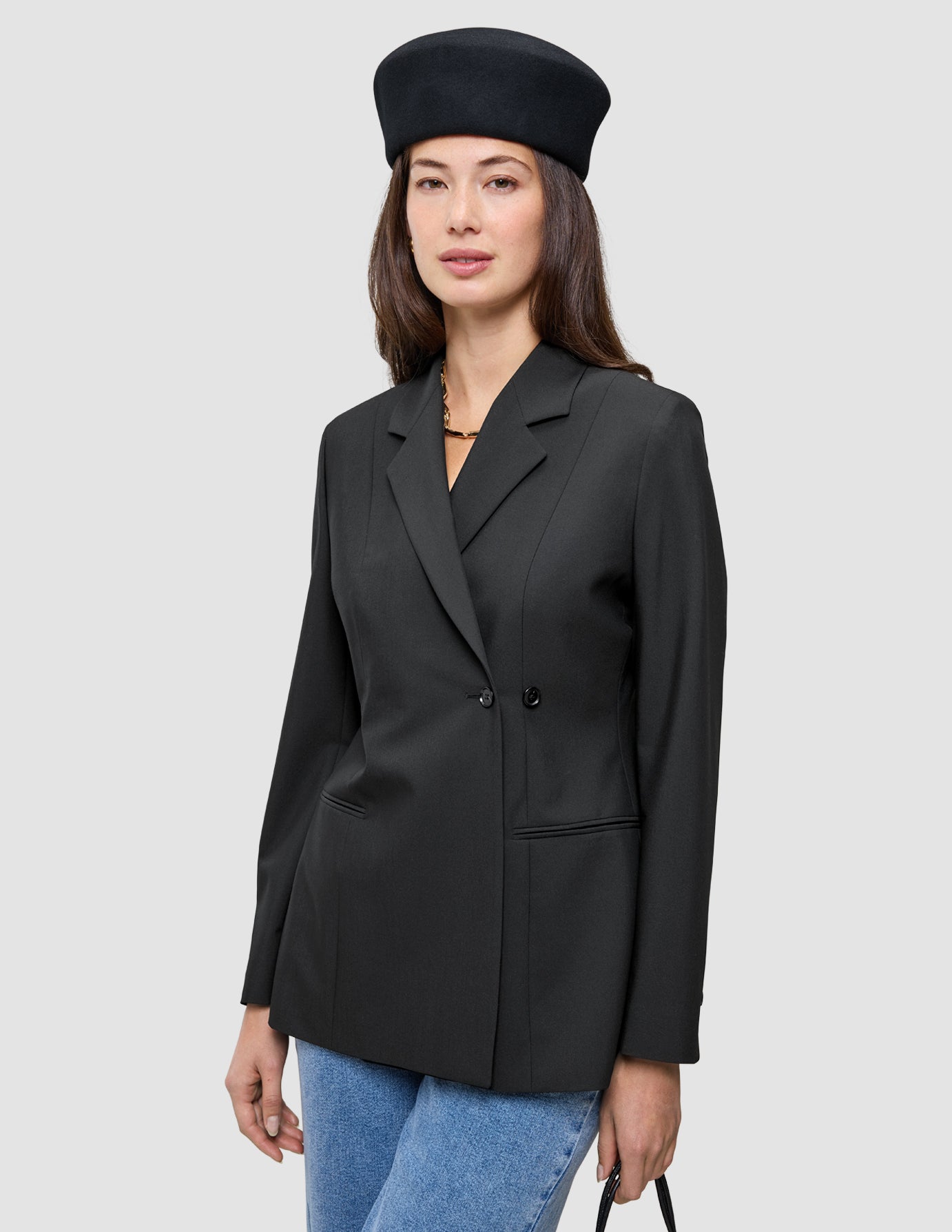 En kvinne som har på seg en svart Women’s Avira Blazer Black med dobbeltradet snitt og en svart beret.