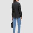 Bakfra-bilde av en person som har på seg en svart Women’s Avira Blazer Black, lyseblå jeans og mørke høyhælte sko, og som holder en håndveske.