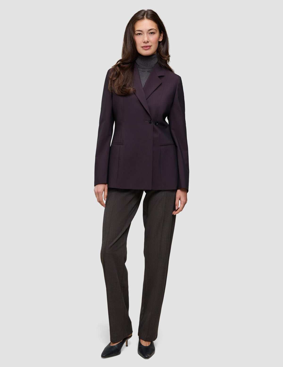 En kvinne som har på seg en Women’s Avira Blazer Burgundy Berry over en grå turtleneck og mørke bukser med svarte høyhælte sko.