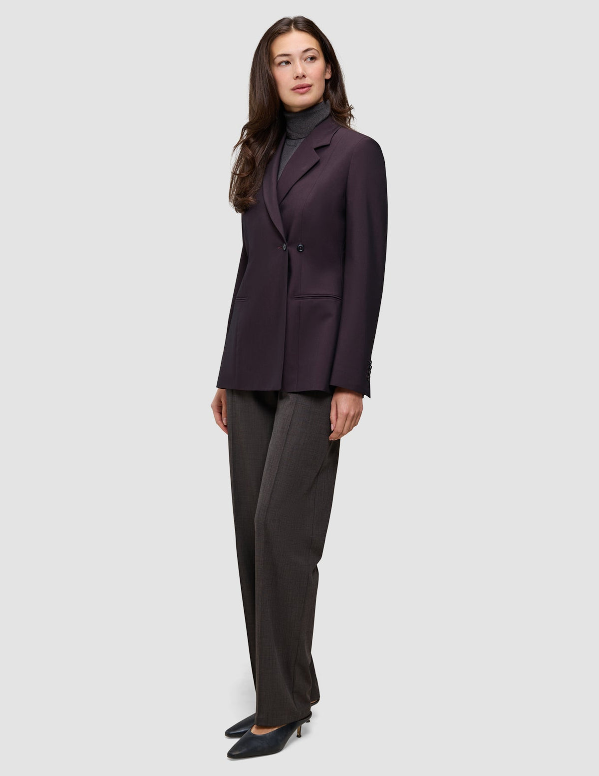 En kvinne har på seg en burgunderfarget Women’s Avira Blazer Burgundy Berry over en grå turtleneck og mørke bukser fra Dansk Design.