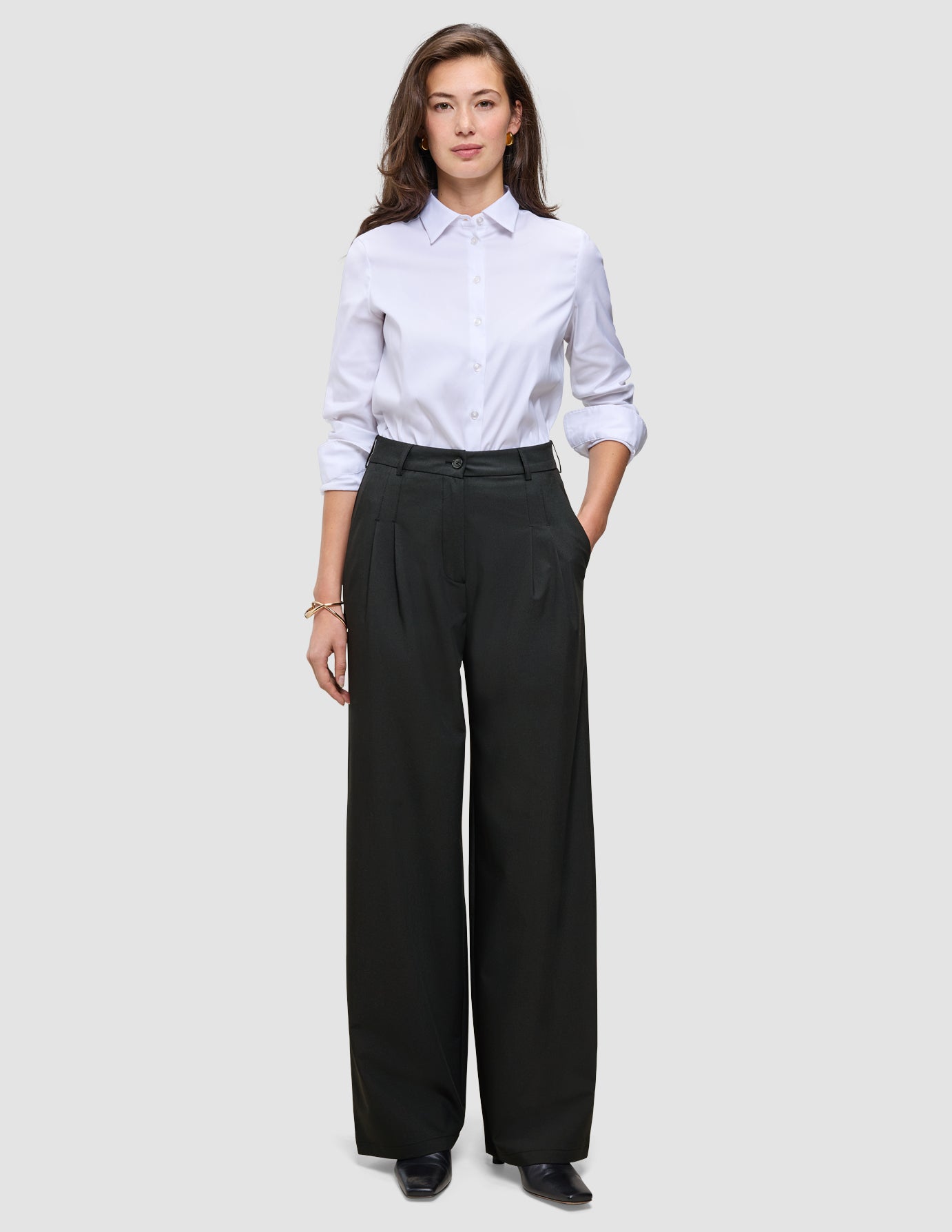 En person som har på seg en hvit skjorte med knapper, stappet inn i et par Women’s Avira Pants Wide Black.